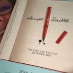 A person holds a book titled "Script & Scribble: The Rise and Fall of Handwriting" by Kitty Burns Florey, with a red pen drawn on the cover, illustrating the nuances of handwriting.