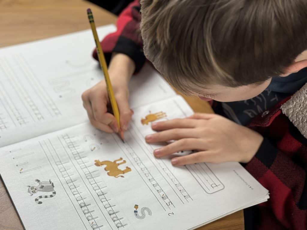 Child practicing handwriting in a workbook with a pencil, focusing on animal-themed exercises.
